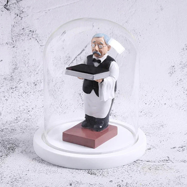 Decorative watch display stand featuring a vintage butler figurine under a glass dome with a white base.
